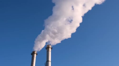 Chimney Stacks Emitting Smoke Against a Blue Sky