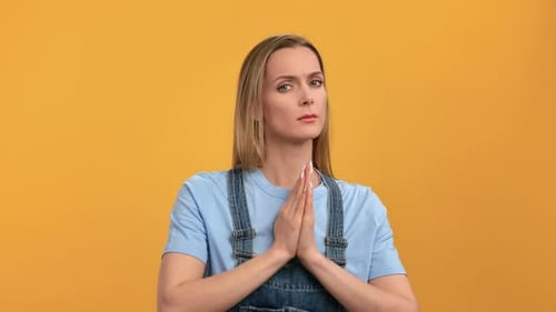 Woman Pleading with Hands Clasped on Yellow Background