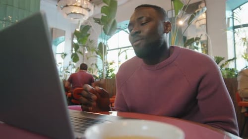 Afro-American Man Chatting via Video Call on Laptop in Cafe