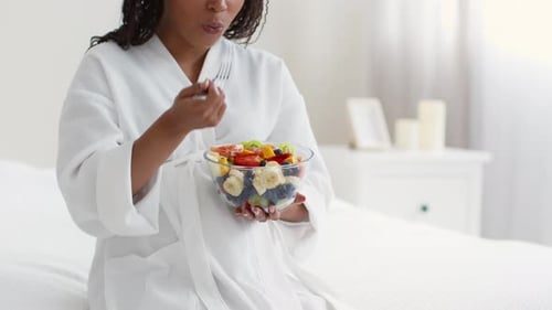 Woman Eating Fruit Salad in White Bedroom