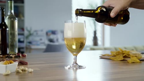 Hand pours beer into a glass on table