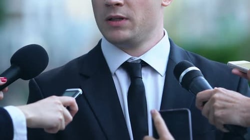 Man in Suit Addresses Press with Microphones