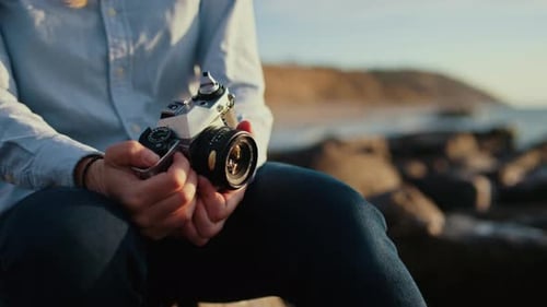 Man Holds Vintage Camera by Ocean at Sunset