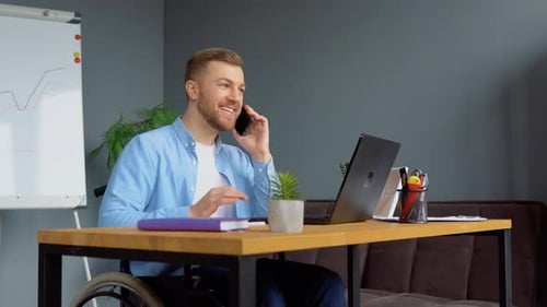 Man in Wheelchair Working at Desk with Laptop