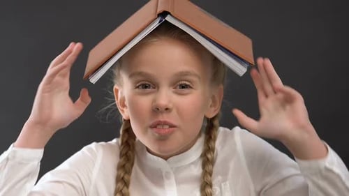 Girl with Book on Head Smiles at Camera