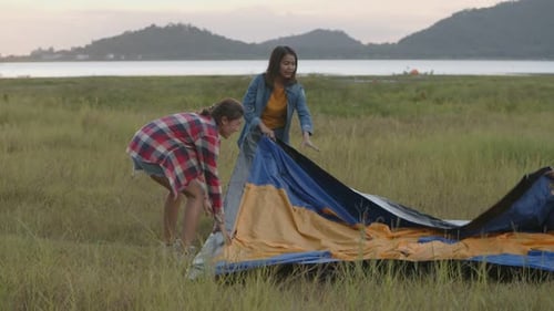 Young Adults Setting Up Tent by Lake at Sunset