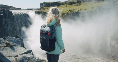 Frau steht am Klippenrand mit Blick auf den Detifoss-Wasserfall in Island