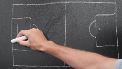 Coach drawing soccer field on blackboard using chalk.