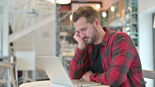 Tired Young Man with Laptop Taking Nap in Cafe