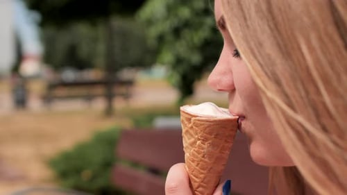 La niña se come un cono de helado en la calle de la ciudad