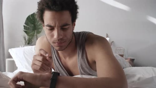 Man Uses Phone and Smart Watch in Bed