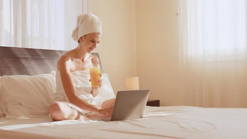 Woman with Laptop and Juice on Bright Morning Bed