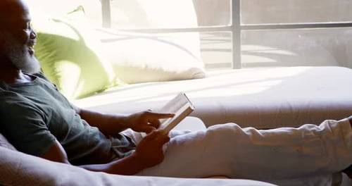 Senior man reading a book in living room 4k