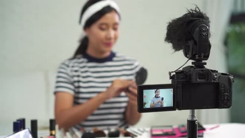La bloguera de belleza presenta cosméticos de belleza mientras está sentada frente a la cámara para grabar un vídeo con un cepillo.