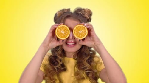 Smiling Woman Plays with Orange Slices on Yellow