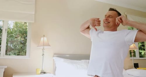 Man Stretching and Yawning in Bright Bedroom in the Morning