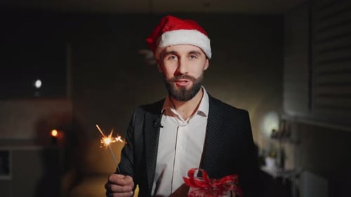 Man in Santa Hat Holds Sparkler and Gift