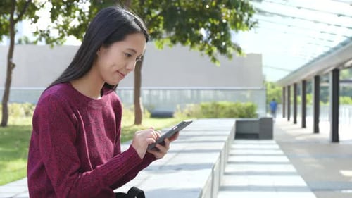 Woman Using Smartphone in Sunny Urban Park
