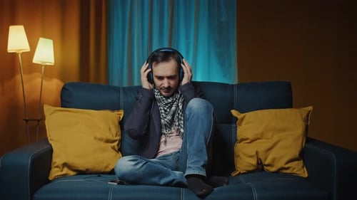Calm Young Man Wearing Wireless Headphones Chilling Listening to Music Sit on Sofa Happy Relaxed