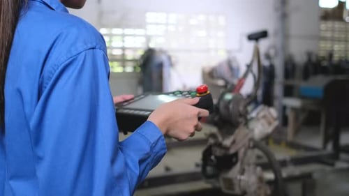 De cerca, las manos de una mujer trabajadora de una fábrica controlan una máquina de brazo robótico industrial mediante el uso de un controlador