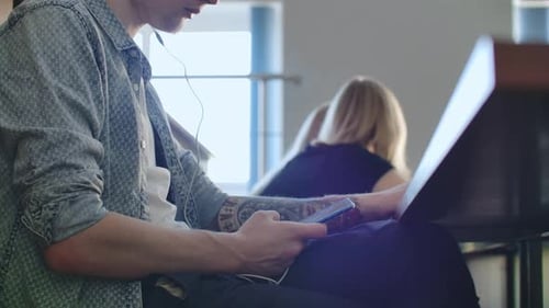 Ein männlicher Student in einem Auditorium der Universität hört während einer Pause Musik in weißen Kopfhörern