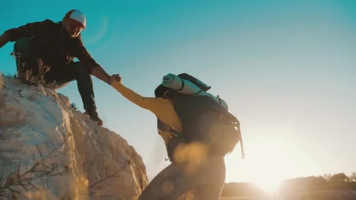 Man Helps Woman Climb Up Rocky Hill