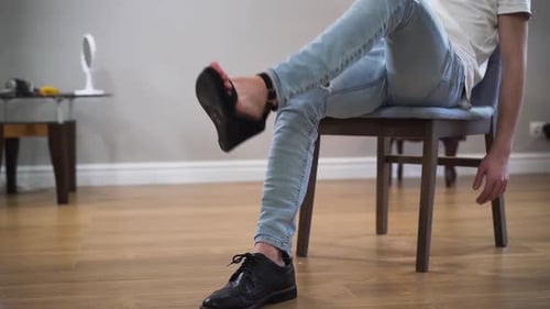 Unrecognizable Caucasian Man in Casual Clothes Sitting on Chair with One Foot in Men's Boot and