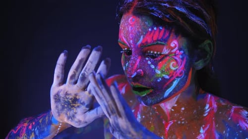 Portrait d'une fille avec un motif UV sur son visage, elle bouge lentement ses mains.