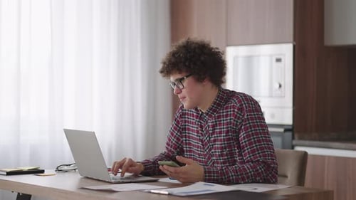 Young Adult Working on Laptop and Holding Smartphone