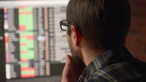 Close Up Back View of Caucasian Male in Glasses Looking at Monitor Wth Spreadhseets and Program