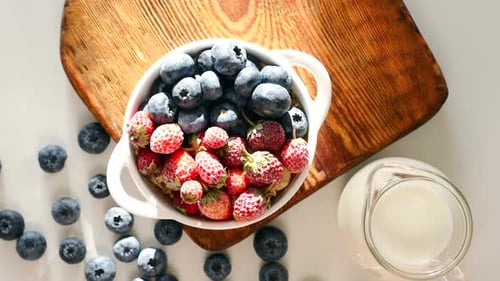 Cup with Blueberry and Strawberry on Wooden Table with Jar of Milk in Sunshine