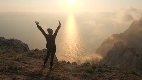 Silhuette Young Woman Arms Outstretched Observing a Beautiful Dramatic Sunset Above a Sea From a