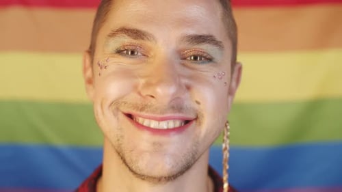 Smiling Young Adult Poses in Front of Pride Flag