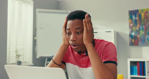Young Darkskinned Boy Sits Slumped in Front of Computer Props Hands Under Face Bad News Losing Money