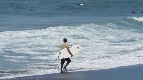 Young Surfer Walking on the Beach with his Surfboard under his Arm