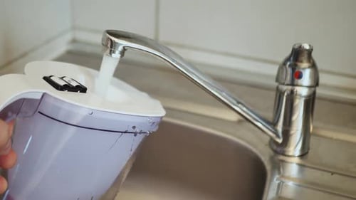 Man Filling Water Filter Jug in the Kitchen