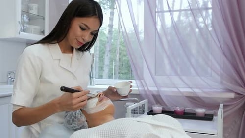 Esteticista sonriente aplicando una mascarilla de arcilla con un cepillo