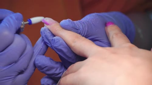 Manicure master in blue gloves removes gel polish from nails using a cutter.