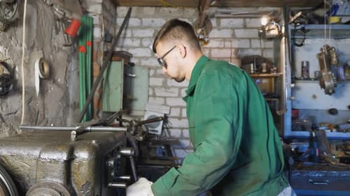 Male Mechanic in Protective Glasses Uses a Turning Lathe to Processing Metal in Workshop