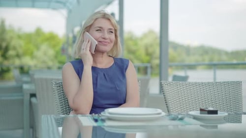Portrait of Positive Adult Caucasian Woman Talking on the Phone As Sitting at Restaurant Table