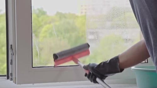 Person Cleaning a Window with Squeegee and Gloves