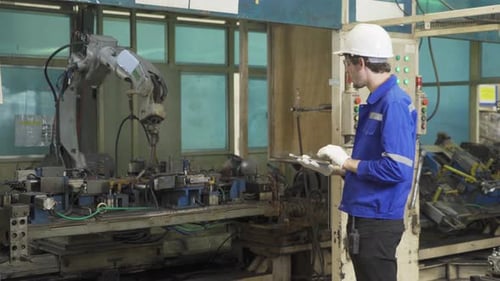 Engineer Inspecting Automated Robot with Tablet in Factory