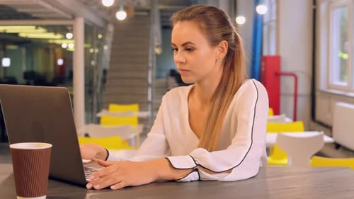 Beautiful Blond Girl Freelancer Is Working on Laptop in Cafe