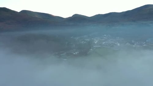 Aerial view of a lake and town covered by fog and clouds at sunset