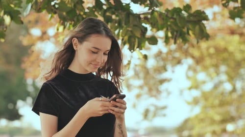 A Young Blonde Russian Girl Writes a Message on the Phone in a Summer Park