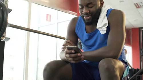 Smiling Afro-American Man Sitting at Gym and Making Video Call on Smartphone