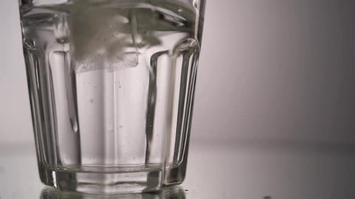 Close Up Ice Falls in a Glass of Water Slow Motion. Morning Light on the Floor Where a Transparent