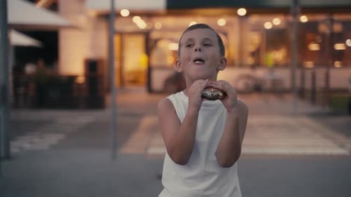 Hungry Young Boy Eating a Burger on the Evening Street