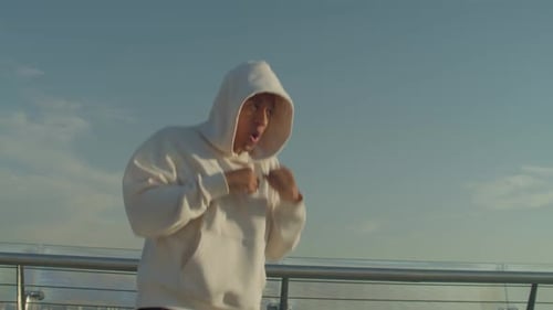 Man in Hoodie Shadow Boxing on City Bridge