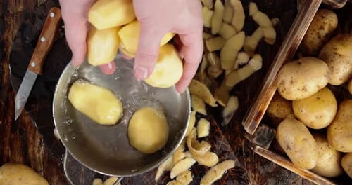 Homens manuais colocam batatas descascadas em uma panela com água.